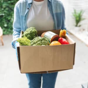 Woman carrying box of garden produce and canned good to donate.